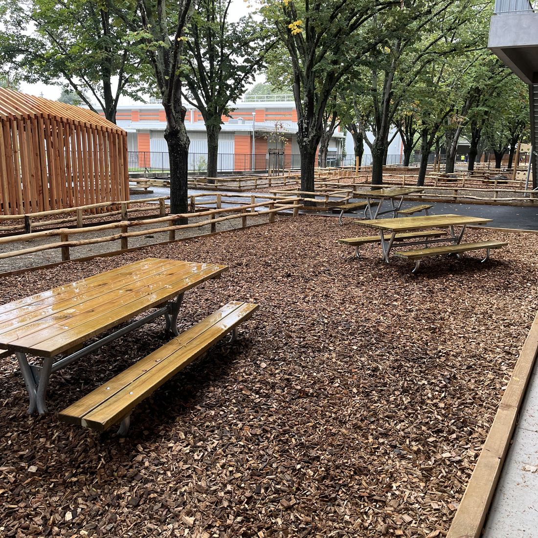 Tables de pique-nique en bois installées sur sol en copeaux dans un espace public ombragé